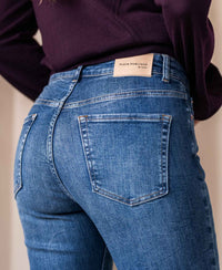 Close-up of a person wearing blue stretch denim flared jeans in stonewash, showing back pocket.