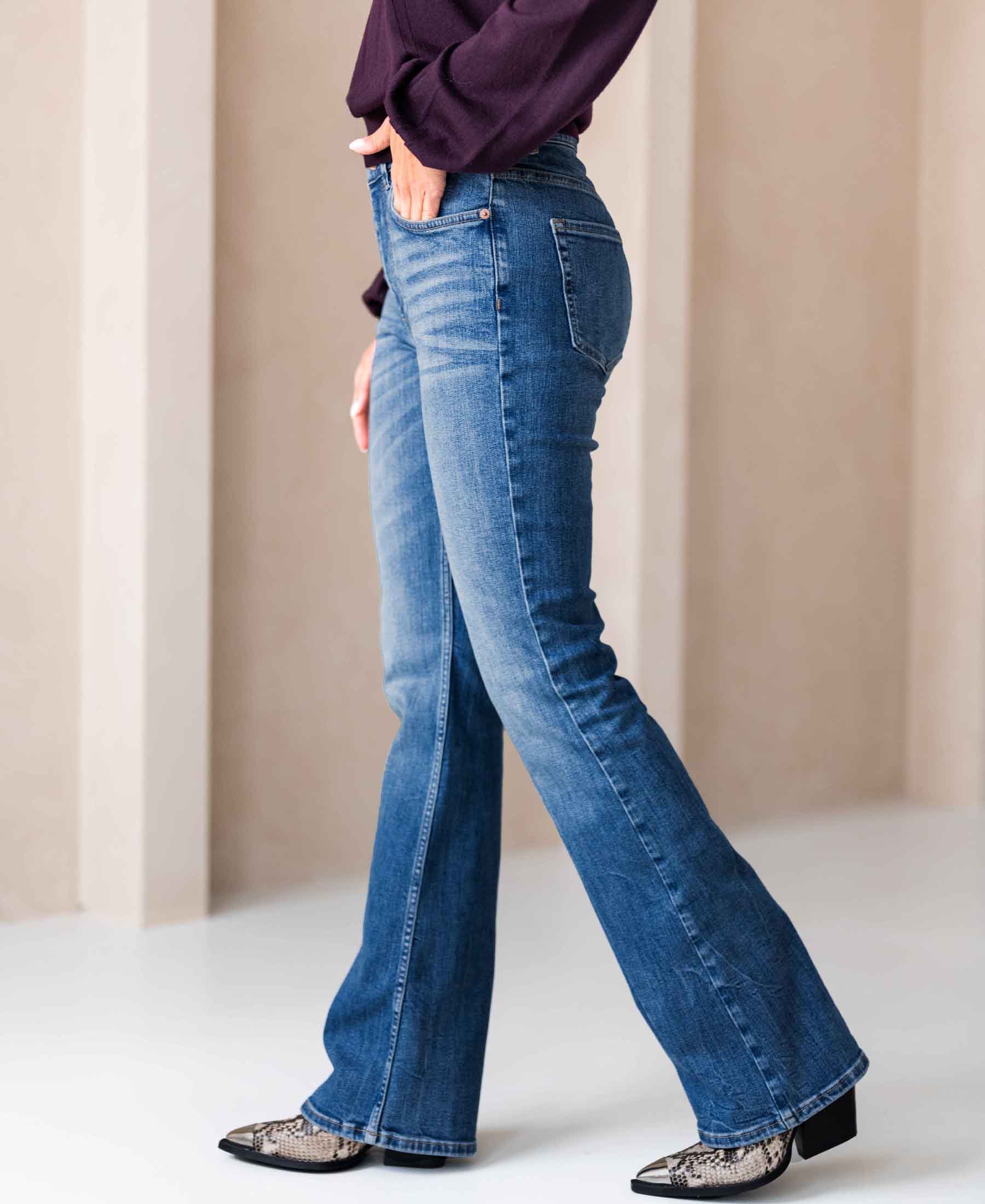 A person wears flared stonewash jeans by a light wall.