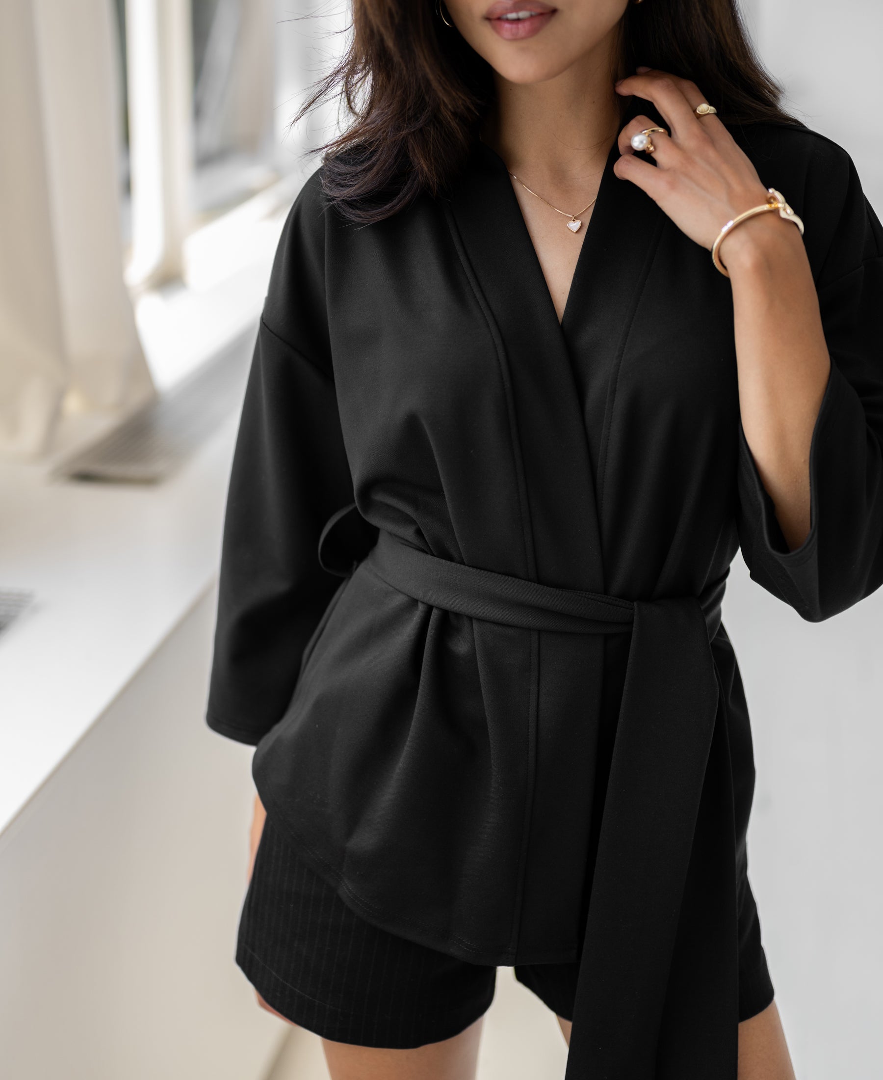 Black LA TOKYO kimono wrap jacket shown worn, viewed indoors by a window with natural light.