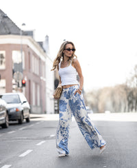 Woman wearing floral print summer pants crossing a city street.