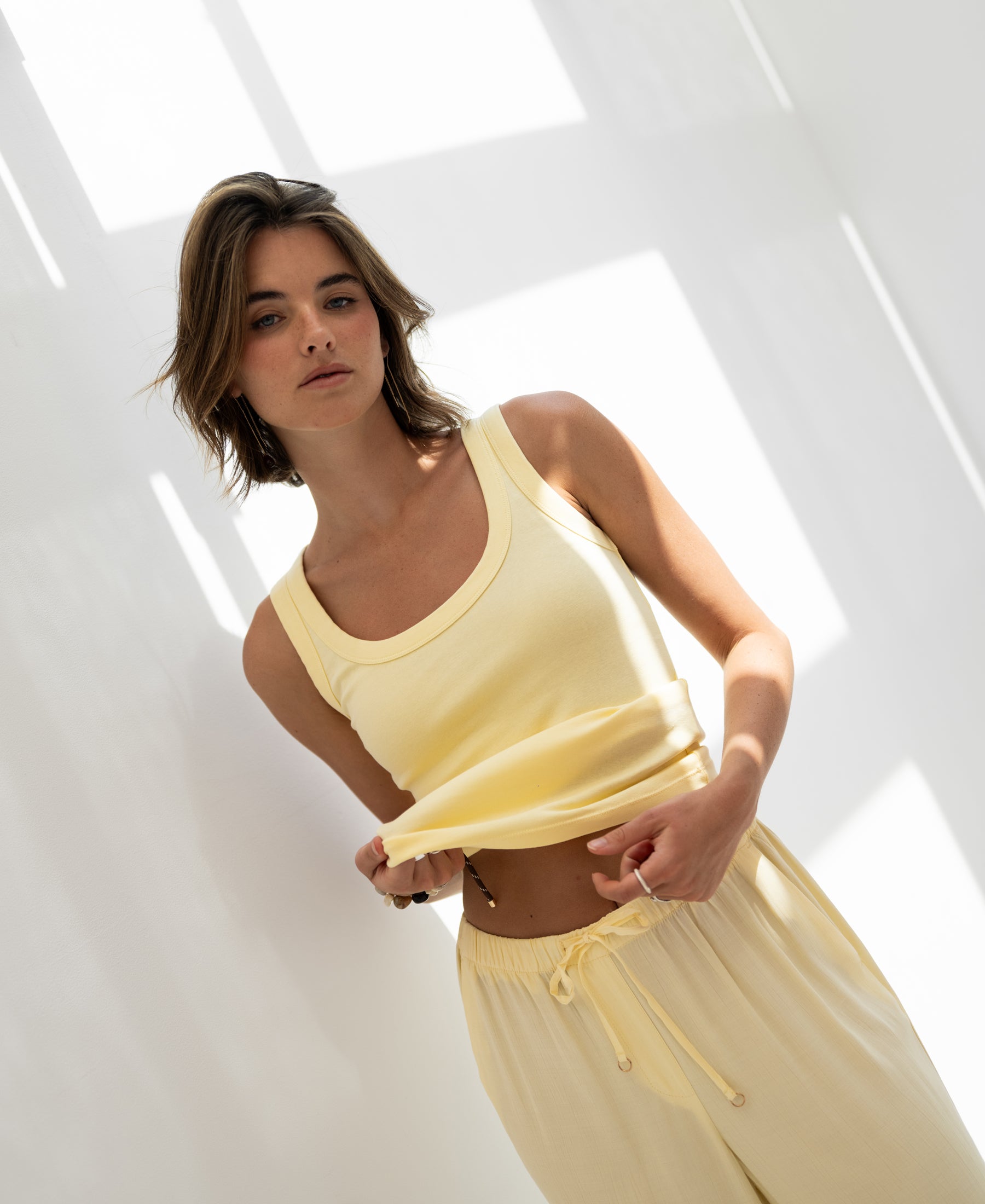 Zacht yellow rib jersey tank top in sunlight, shown from the front, model holding shirt with a neutral expression.