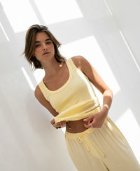 Zacht yellow rib jersey tank top in sunlight, shown from the front, model holding shirt with a neutral expression.