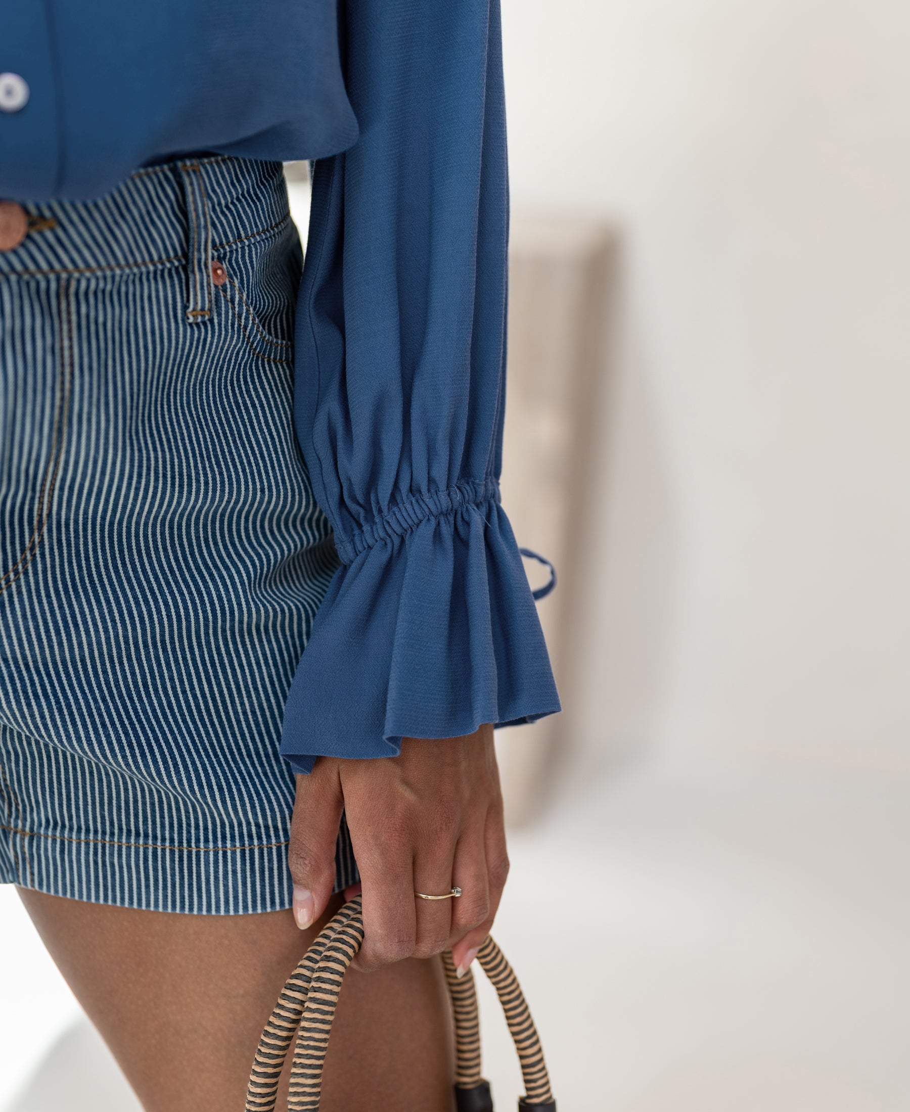 Torso view of a person wearing the PLEIN PUBLIQUE LA TROYES blue blouse; hand and part of woven handbag visible.