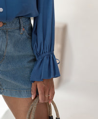 Torso view of a person wearing the PLEIN PUBLIQUE LA TROYES blue blouse; hand and part of woven handbag visible.