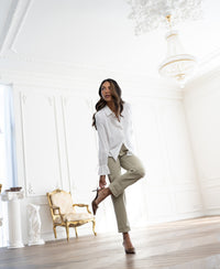 Woman wearing a white LA TROYES blouse by PLEIN PUBLIQUE stands in a bright, ornately decorated room.