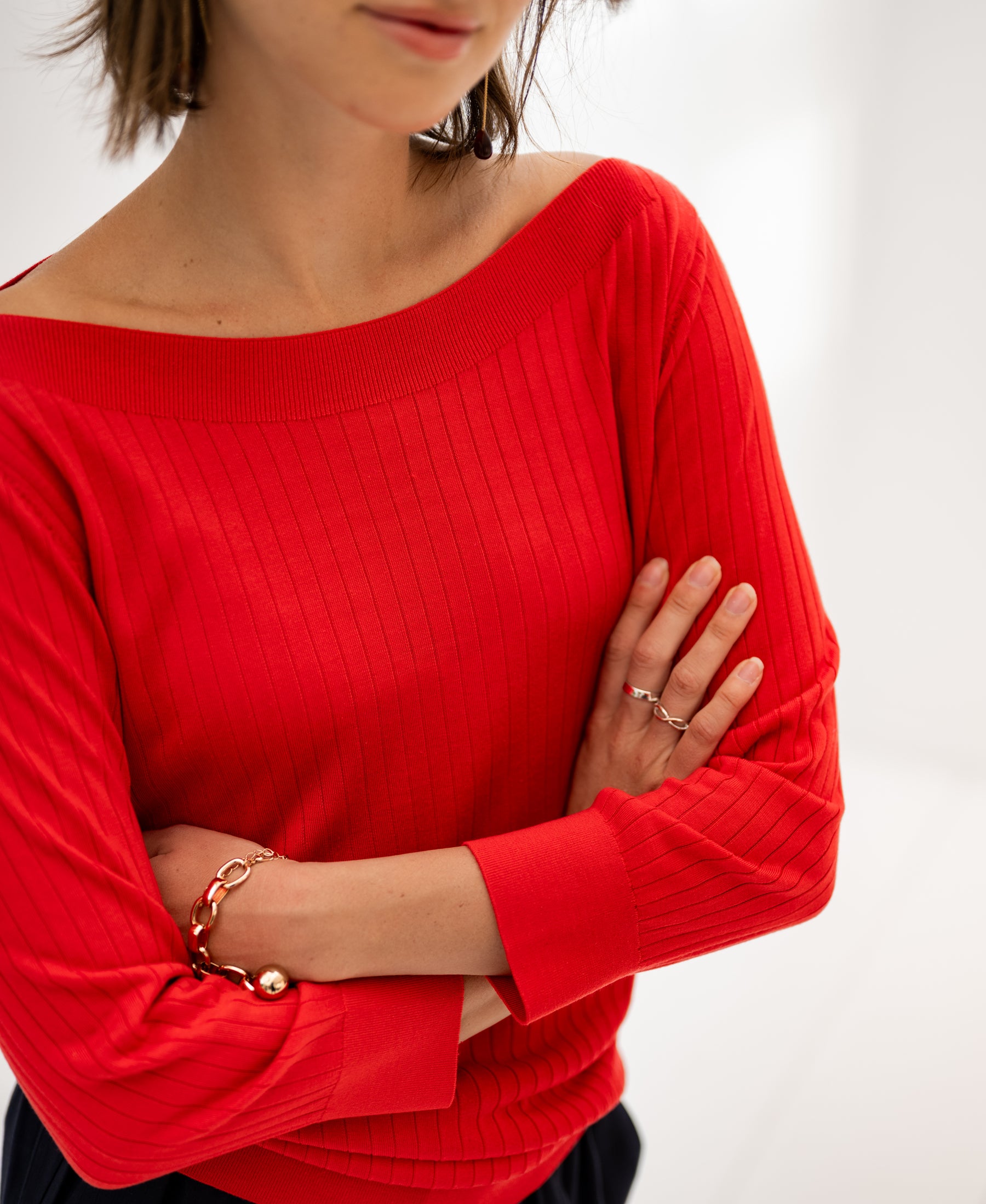 Coral red Tencel-silk boat neck sweater, arms crossed, shown in a bright room.