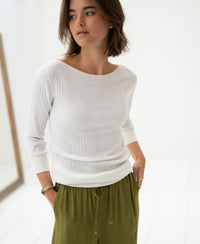 Woman wearing a white Tencel-silk boat neck sweater in a bright, minimalist room.