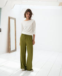Woman wearing a white Tencel-silk boat neck sweater stands by a mirror in a bright room.
