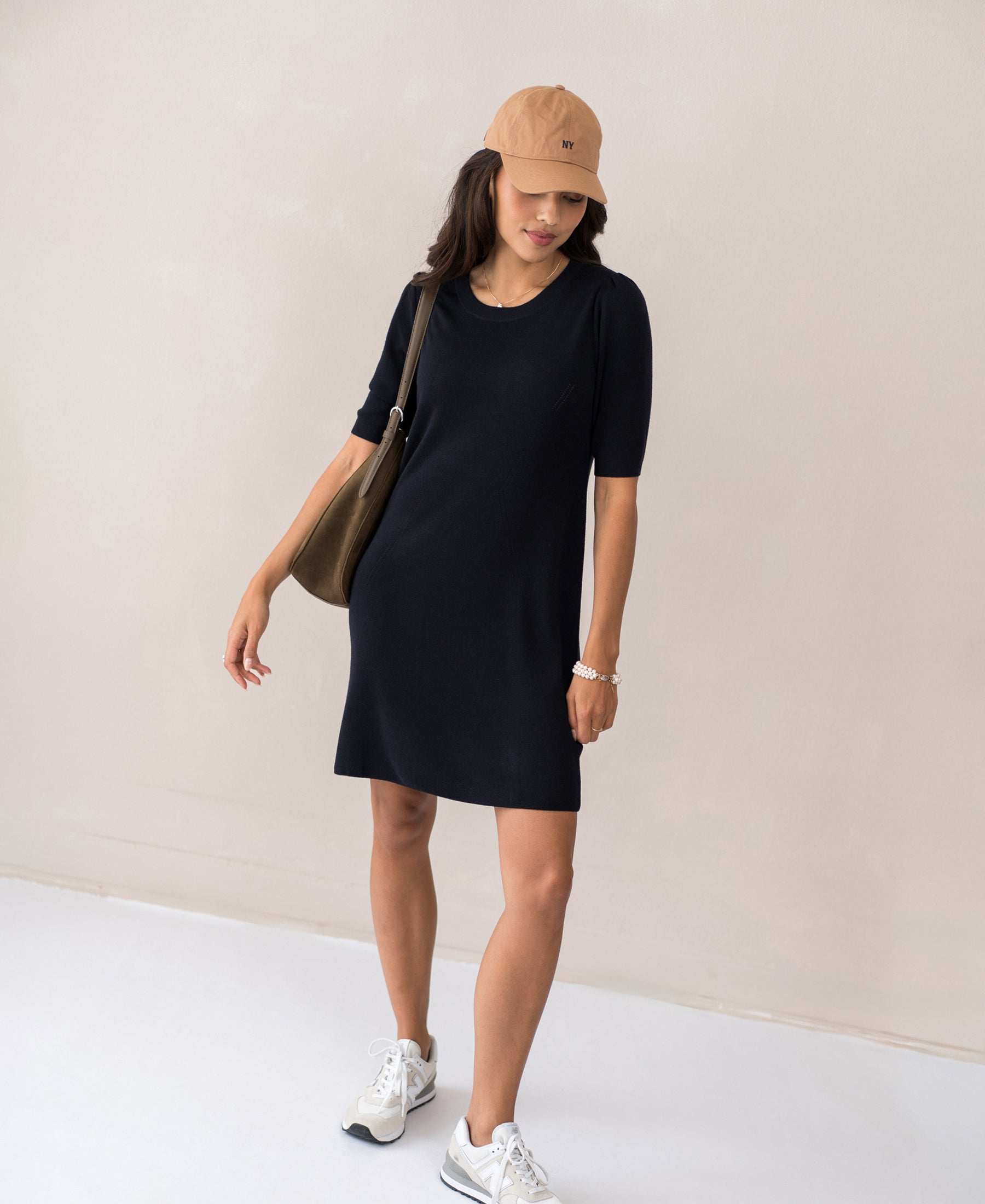 Woman wearing a PLEIN PUBLIQUE merino wool dress LA TWIGGY in dark blue standing by a beige wall.