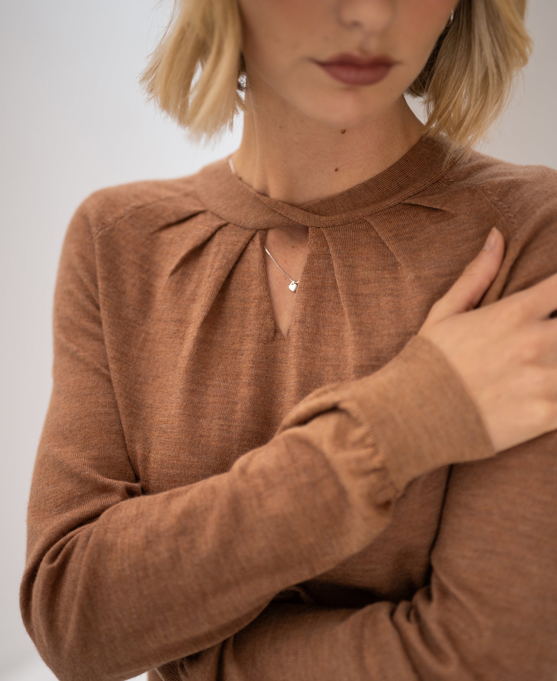 Woman wearing a PLEIN PUBLIQUE merino wool sweater, LA TWIST in Chai tea color, left arm crossed.