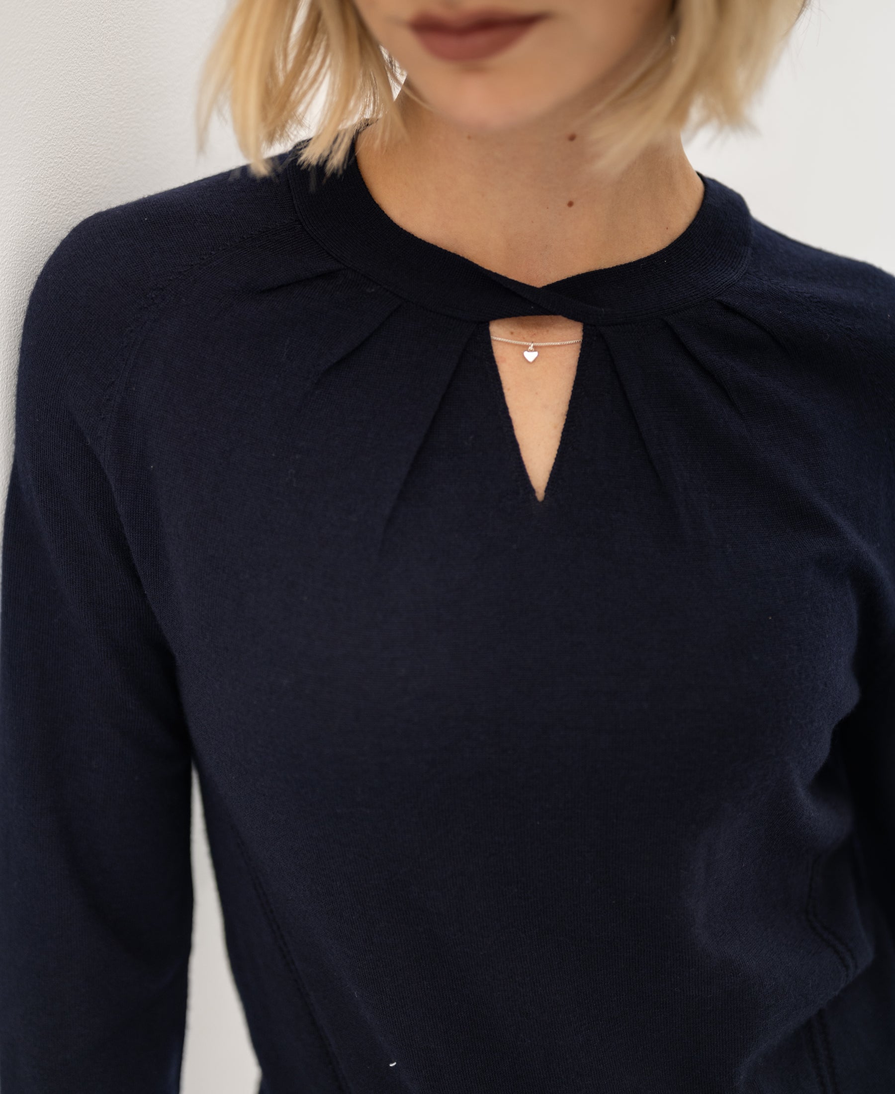Navy blue PLEIN PUBLIQUE LA TWIST merino wool sweater with keyhole neckline and small chain, shown from shoulders to lips.