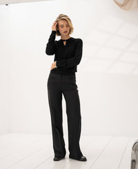 Black merino wool sweater with twist detail, shown in a bright, minimalist room.