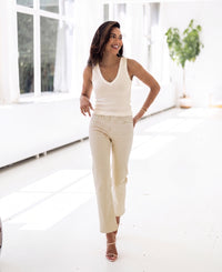 Woman wearing a soft butter-colored luxury knit top walks in a bright room with large windows.