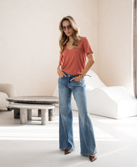 Woman wearing OVERIG’s bamboo T-shirt in bright terra color, standing with hands in pockets.