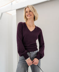 Woman wearing a PLEIN PUBLIQUE Merino wool V-neck sweater in aubergine, shown indoors.