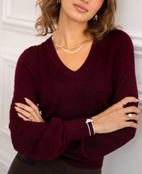 Merino wool V-neck sweater in Bordeaux red from PLEIN PUBLIQUE, shown indoors with crossed arms.