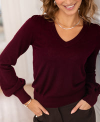 Woman wearing a PLEIN PUBLIQUE Merino wool V-neck sweater in Bordeaux, indoors.