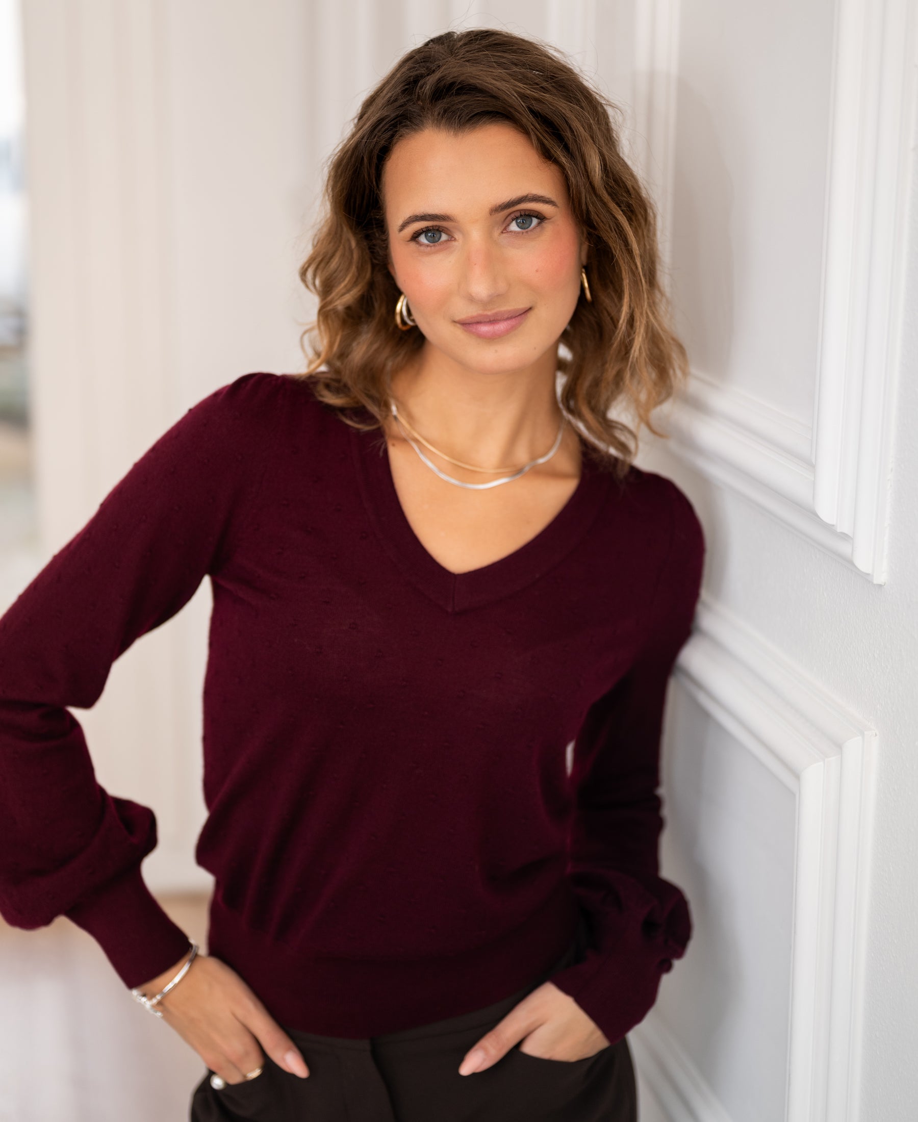 Merino wool V-neck sweater in Bordeaux red from PLEIN PUBLIQUE, shown indoors.