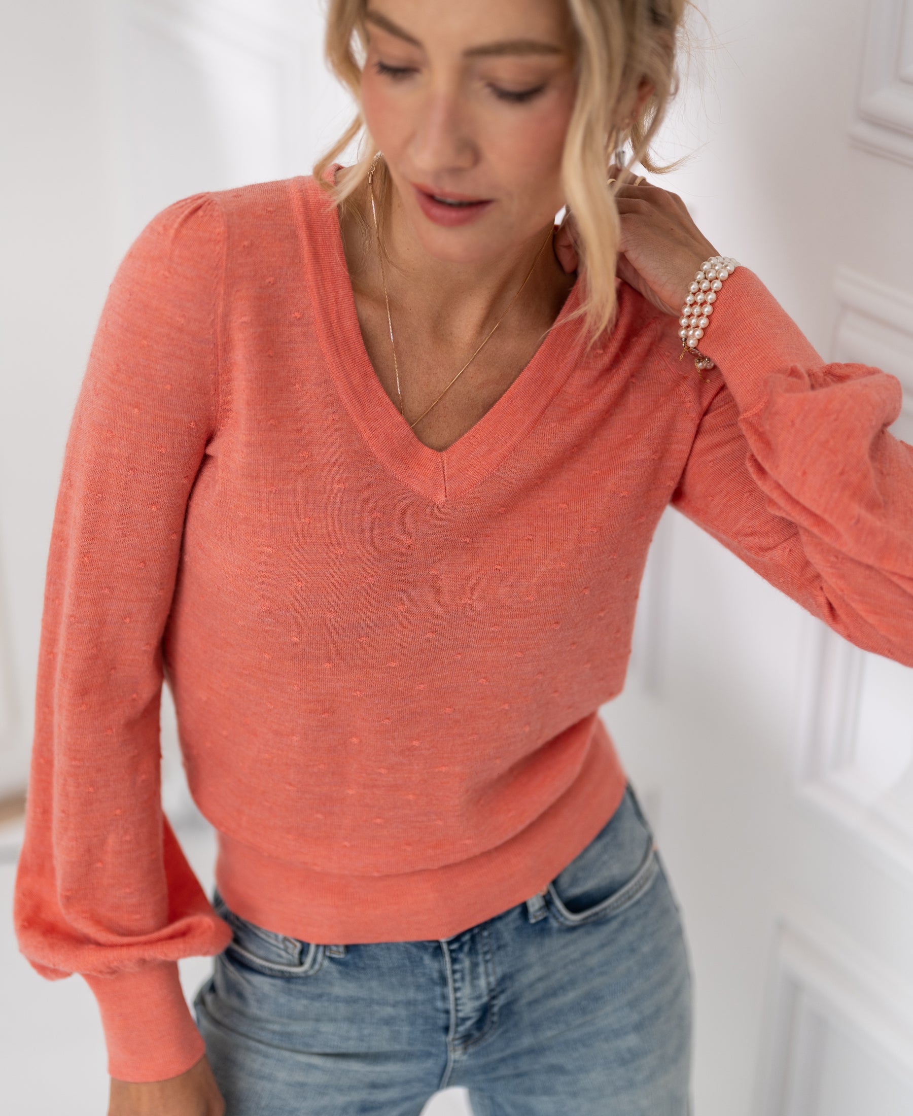 Woman wears PLEIN PUBLIQUE Merino wool V-neck sweater LA VICTORIA in Flamingo pink with puffed sleeves, indoors.