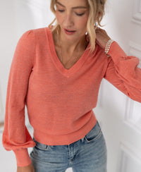 Woman wears PLEIN PUBLIQUE Merino wool V-neck sweater LA VICTORIA in Flamingo pink with puffed sleeves, indoors.