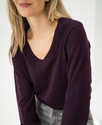 Woman wearing the PLEIN PUBLIQUE Merino wool V-neck sweater LA VILLE in aubergine, smiling.