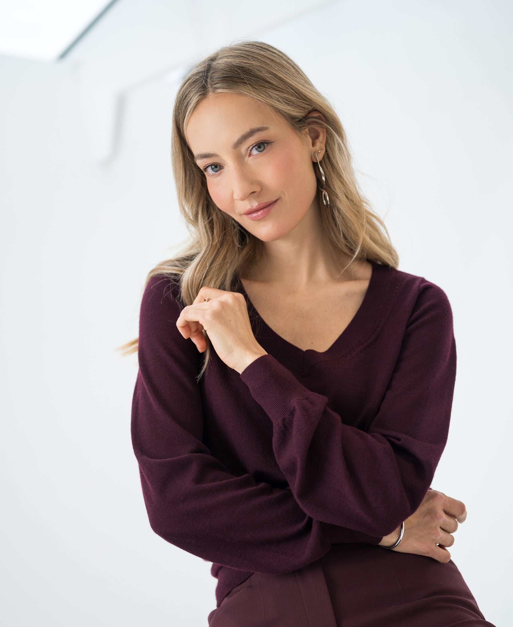 Woman wearing burgundy PLEIN PUBLIQUE Merino wool V-neck sweater indoors.