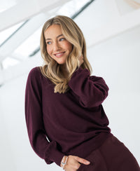 Merino wool V-neck sweater in Bordeaux red by PLEIN PUBLIQUE, shown in a bright space.