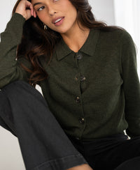 Woman wearing a green collared knit vest, seated with her arm resting on her knee.