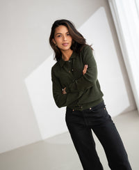 Woman wearing green PLEIN PUBLIQUE polo collar vest, neutral background, soft indoor lighting.