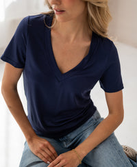 Woman wearing a relaxed fit navy lyocell T-shirt sits indoors, face angled.