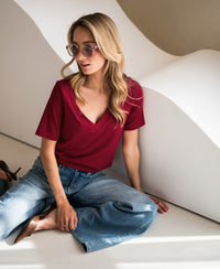 Woman wearing a stretch short-sleeve T-shirt in chili red, sitting by a wavy wall.