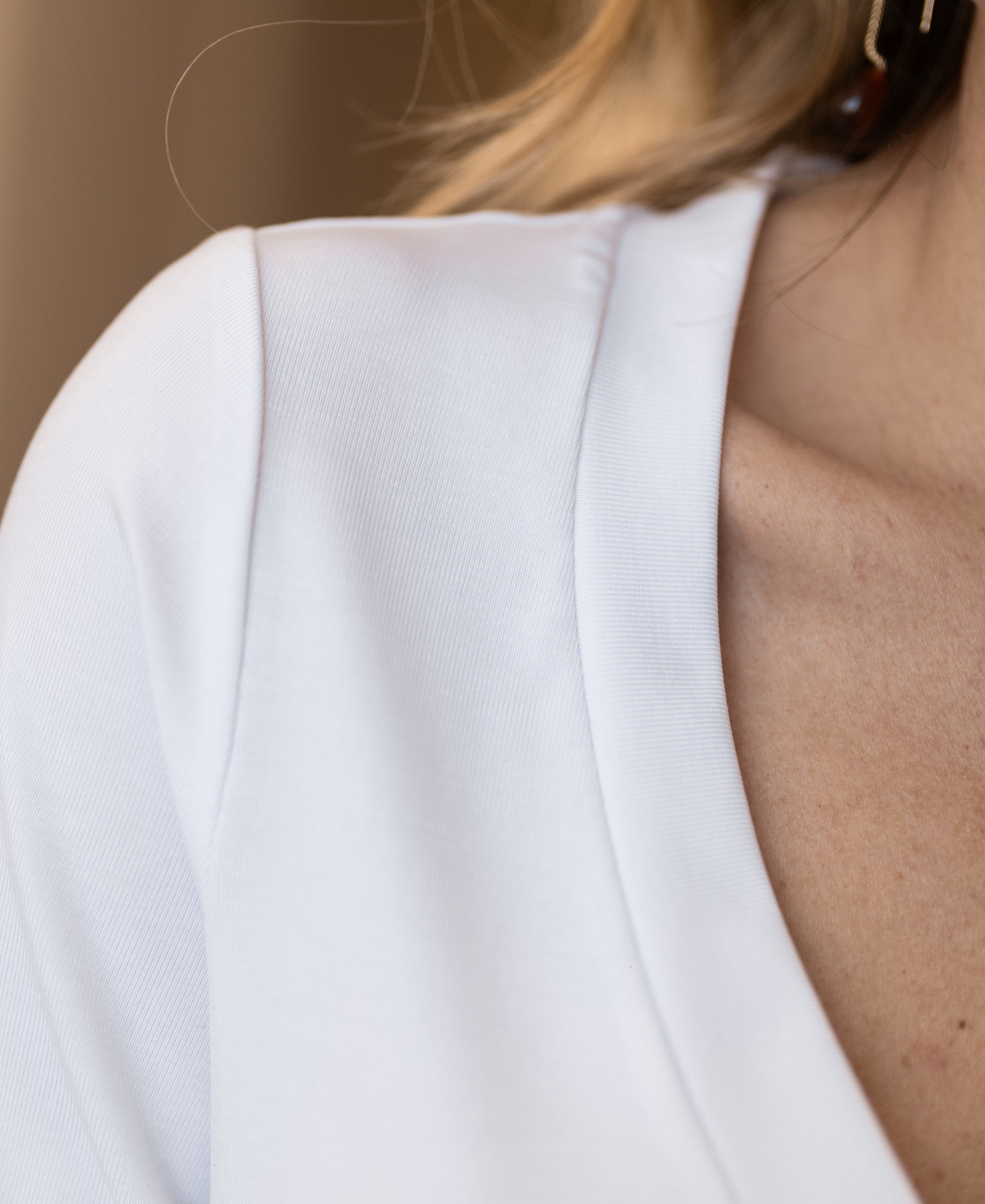 Close-up of a woman's shoulder wearing a white PLEIN PUBLIQUE stretch T-shirt with short sleeves.