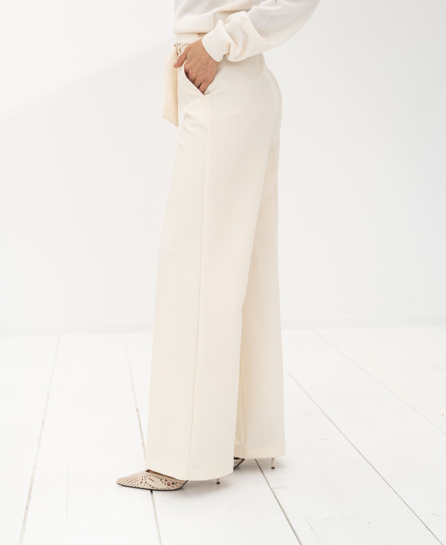 Cream LA WENDE trousers by PLEIN PUBLIQUE, shown on a person standing on a white floor.