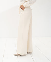 Cream LA WENDE trousers by PLEIN PUBLIQUE, shown on a person standing on a white floor.