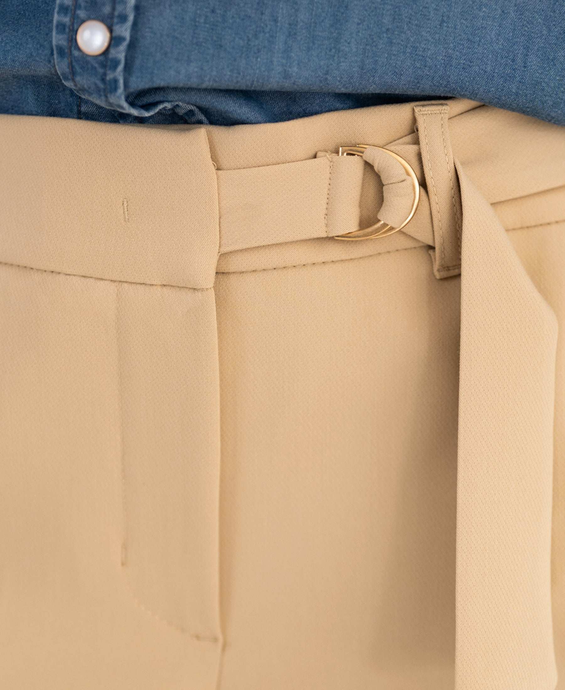 Close-up of beige LA WENDE Pants by OVERIG with asymmetric belt and gold buckle.