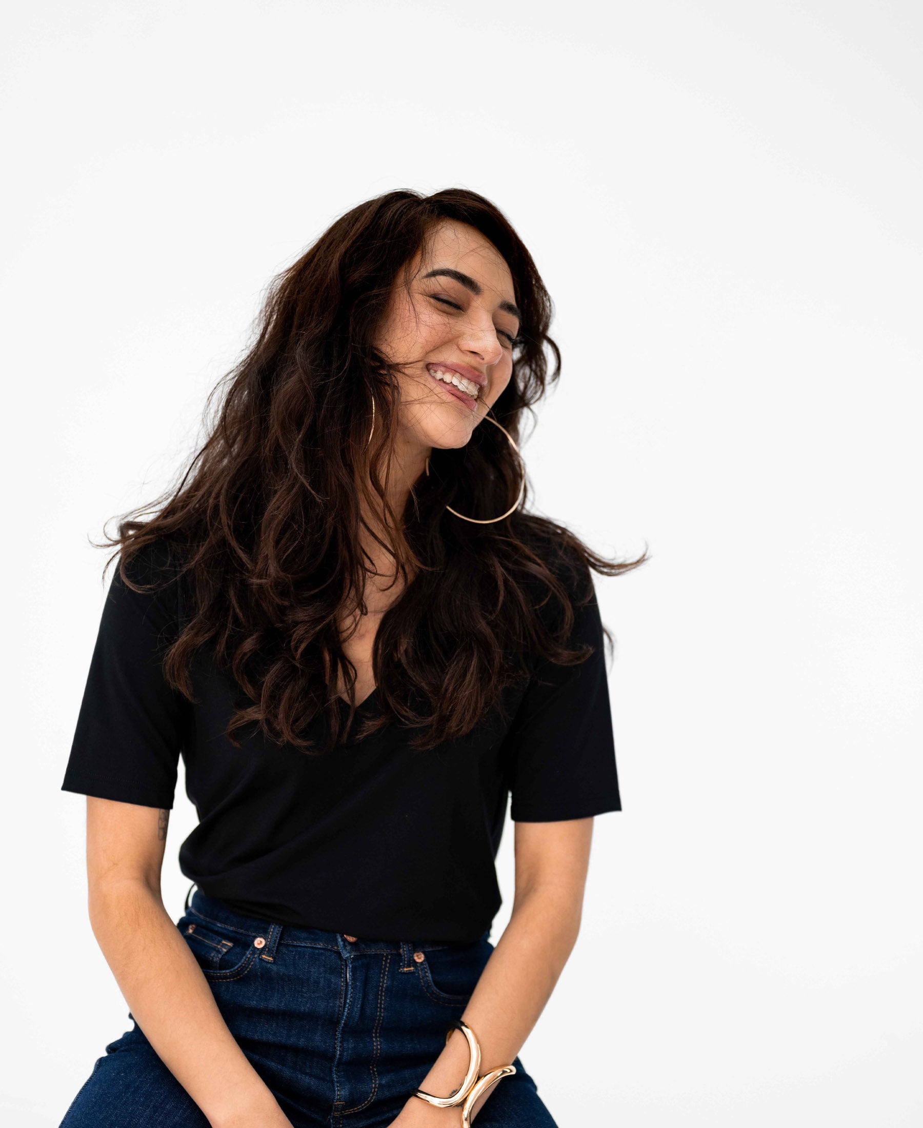 Woman wears the PLEIN PUBLIQUE LA VERONIQUE black V-neck T-shirt, smiling against a white background.