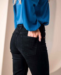 Black denim flare jeans in view from the waist down, one hand in back pocket.