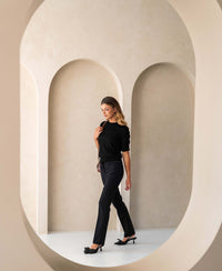 Black merino wool sweater for women, shown in a modern neutral-tone archway interior.