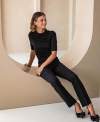 Black merino wool sweater shown on model seated indoors.