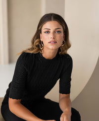 Woman wearing the PLEIN PUBLIQUE LA BRIOCHE black merino wool sweater, looking at the camera.