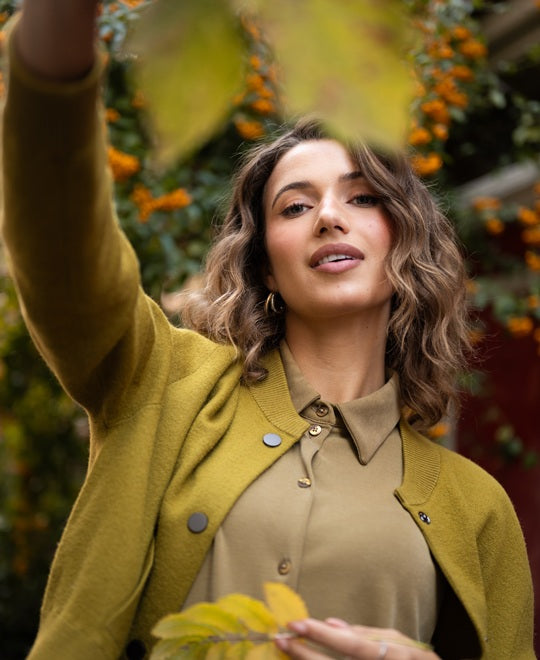 Green sweater shown outdoors, modeled by a woman with wavy hair, standing near orange berries.