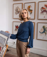 Woman wearing an indigo blue merino wool sweater in an art gallery with animal illustrations.