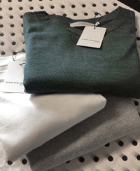 Green merino wool pullover with green, white, and gray tags displayed on a dotted white surface.
