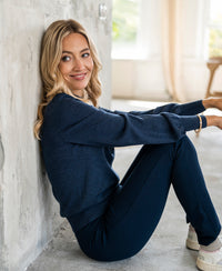 Woman wearing a blue denim turtleneck sweater sits against a concrete wall.