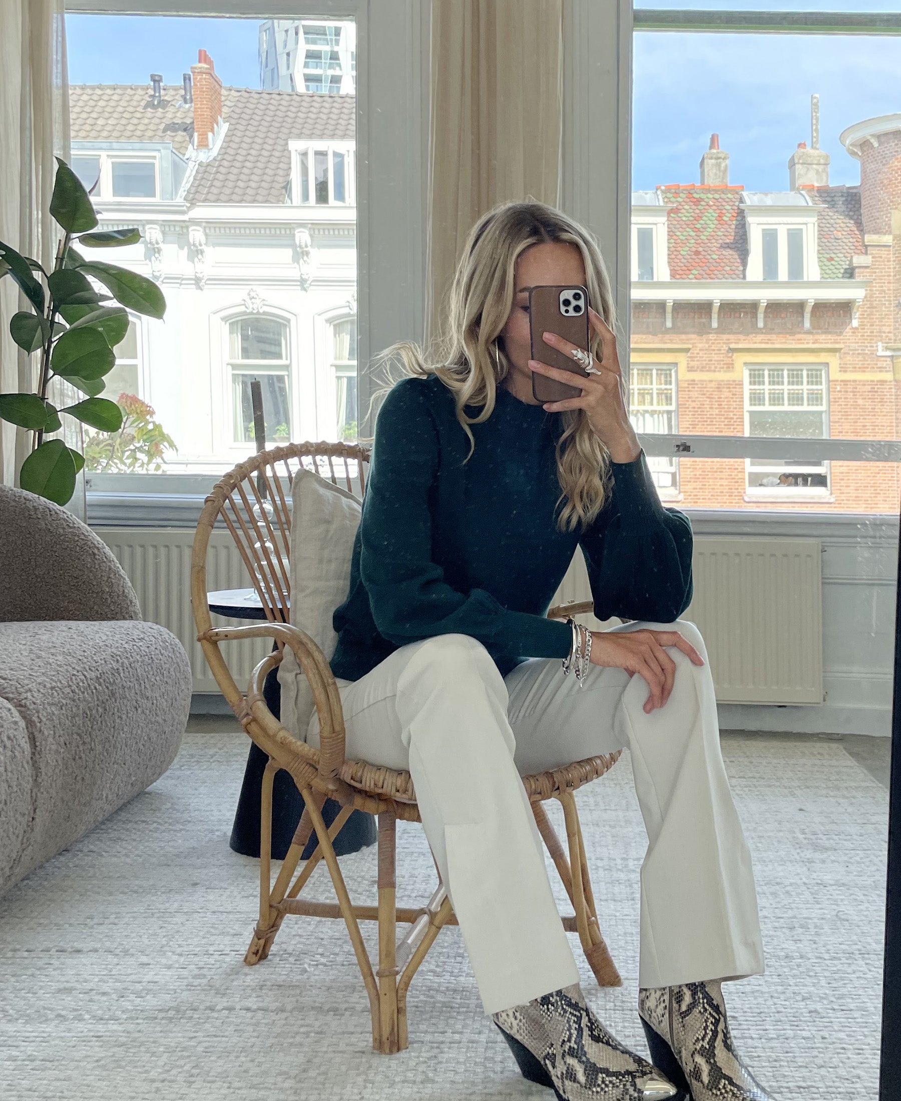 Woman wearing a dark green turtleneck sweater takes a mirror selfie.