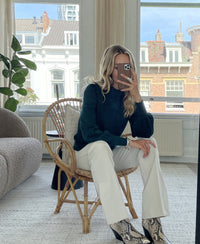 Woman wearing a dark green turtleneck sweater takes a mirror selfie.