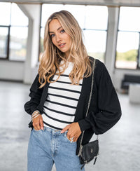 Woman with long blond hair wearing PLEIN PUBLIQUE Breton striped sweater L'ELISA in ivory-black by the window.