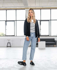 The PLEIN PUBLIQUE Breton sweater L'ELISA in ivory-black, shown worn by a woman in a modern room.