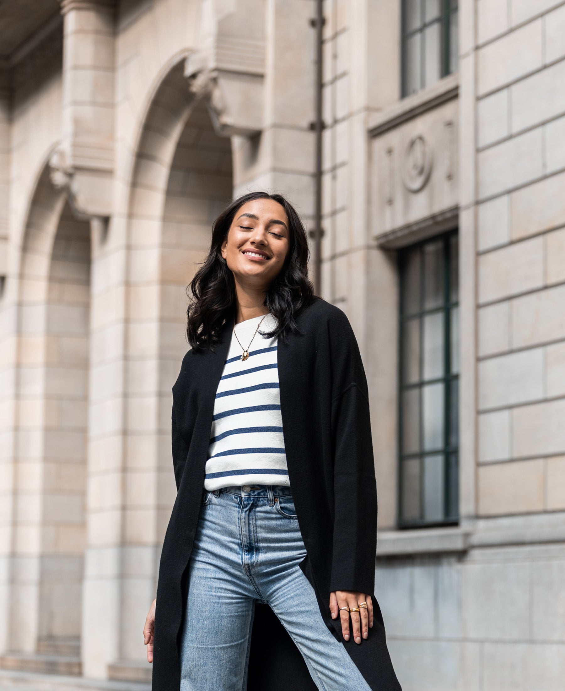 Woman wearing an ivory and denim blue Breton striped sweater by Plein Publique, smiling outside.