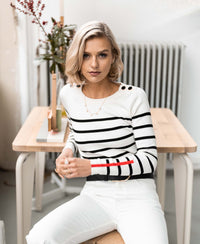 Front view of a woman wearing the PLEIN PUBLIQUE L'ELISA ivory-black Breton sweater, seated at a wooden table.